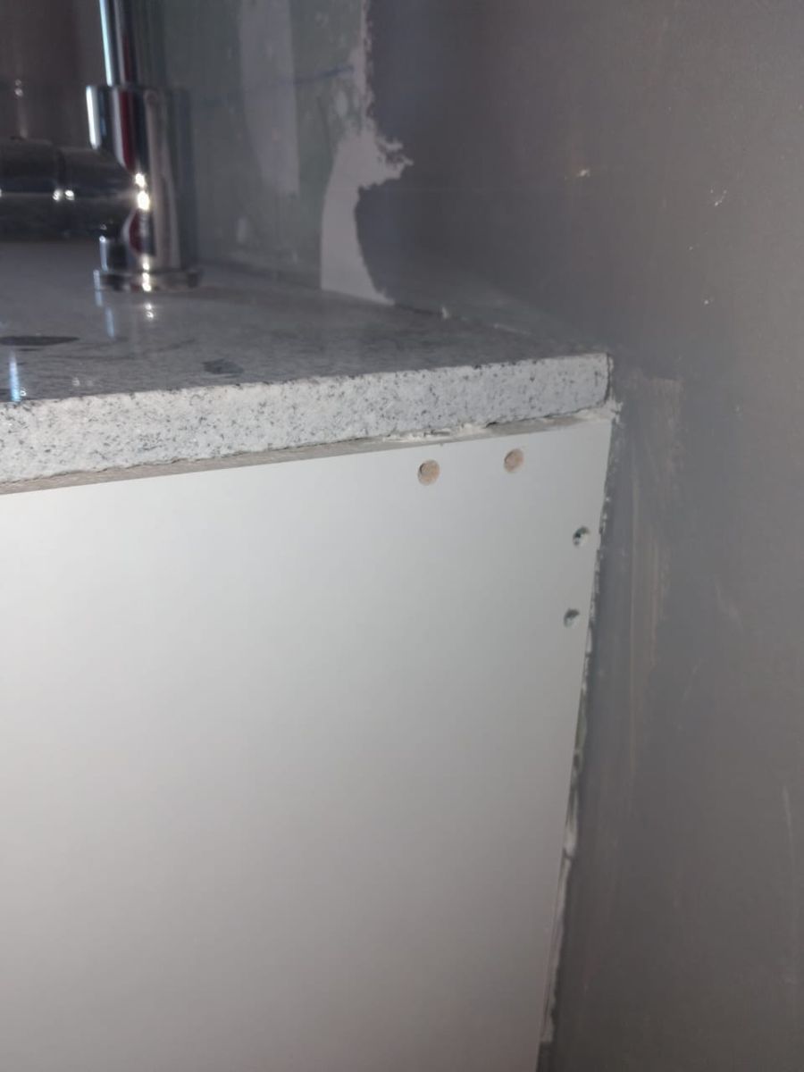 Cubierta de granito sin sello contra el muro y mueble con tornillos a la vista