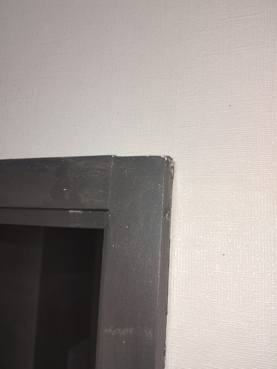 Esquina superior del marco de una puerta gris con las pilastras desalineadas