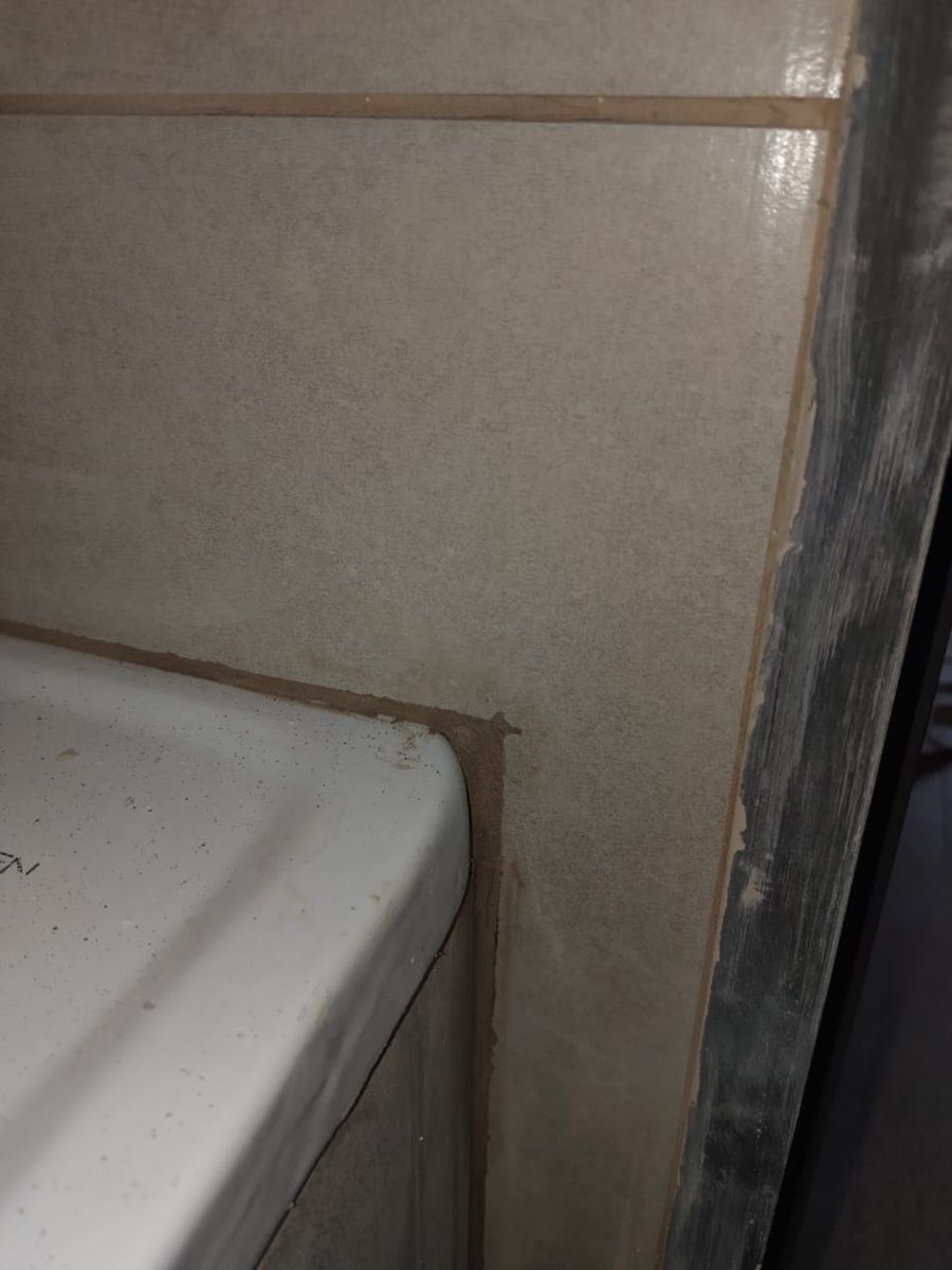 Encuentro entre la tina y el porcelanato del muro con una pieza cortada de más, junto a una pilastra gris sin terminar de pintar